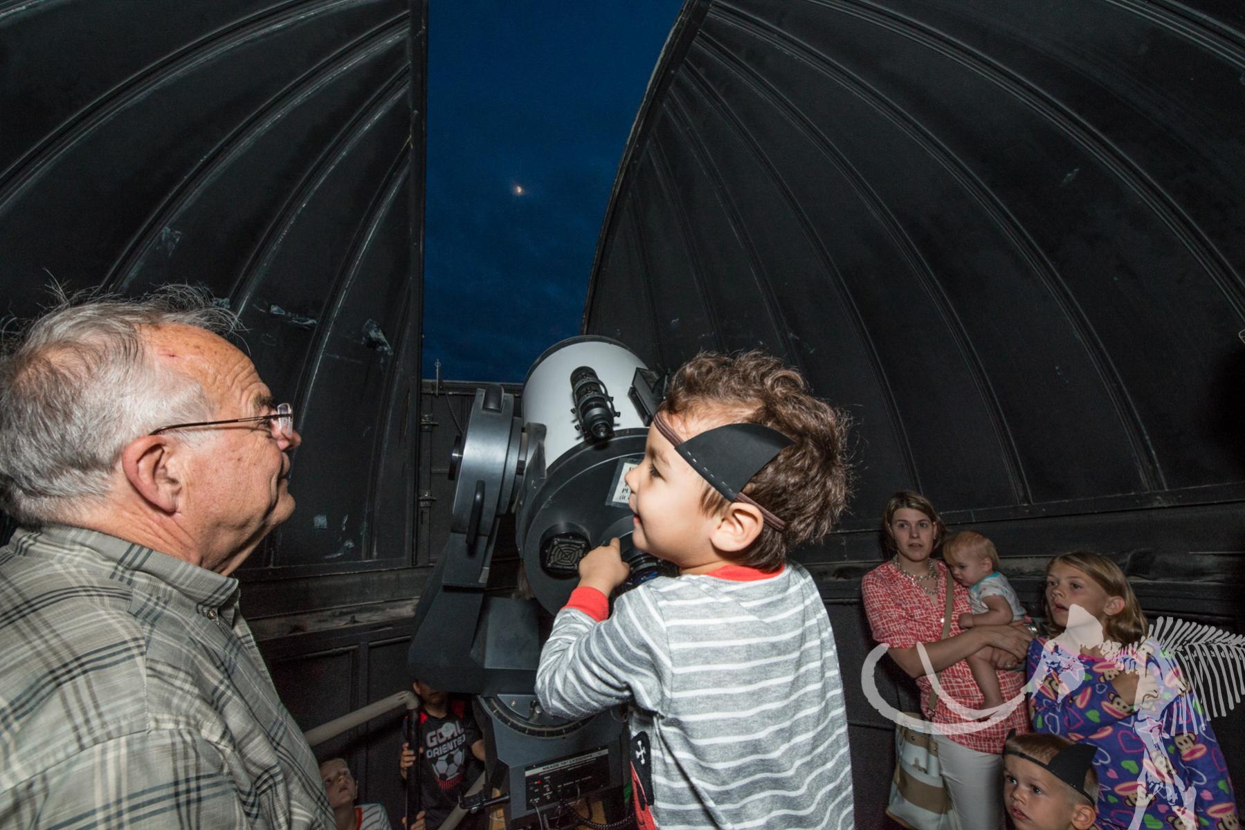 Child holds telescope while Professor Emeritus Ed Schmidt looks on