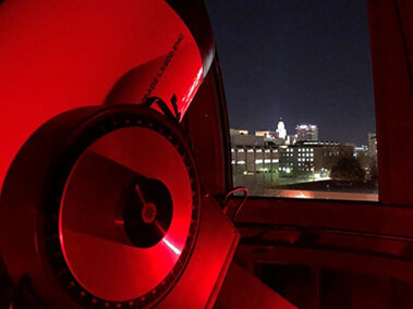 16" Telescope at the Student Observatory illuminated in red light, looking through the slit of the dome to the city.